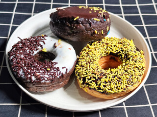 Three delicious donuts topped with sprinkles and various colored glazes, displaying a tempting...