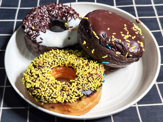 Three delicious donuts topped with sprinkles and various colored glazes, displaying a tempting...