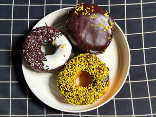 Three delicious donuts topped with sprinkles and various colored glazes, displaying a tempting...