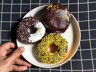 Three delicious donuts topped with sprinkles and various colored glazes, displaying a tempting...