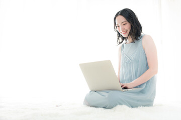 部屋でパソコンの作業をする女性の全身　春夏のノースリーブ白バック