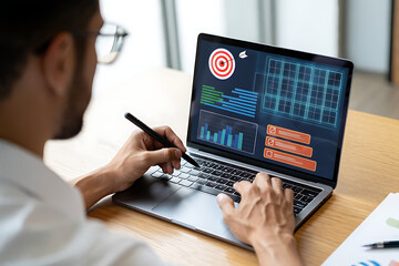 Man analyzing business goals and performance metrics on laptop with stylus and digital dashboard interface