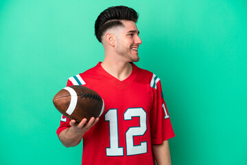 Young caucasian man playing rugby isolated on green background laughing in lateral position