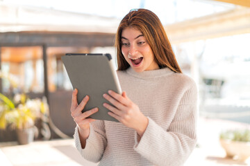 Young pretty caucasian woman holding a tablet with surprised expression