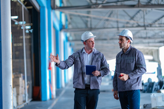 Two logistics specialists discuss warehouse operations with visible shelving and truck access. Modern supply chain teamwork focused on productivity and safety.