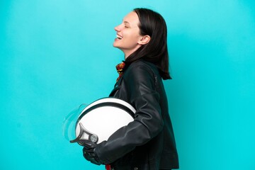 Young caucasian woman with a motorcycle helmet isolated on blue background laughing in lateral...