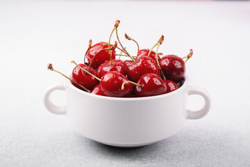 Close‑up cherries in white cup on white for macro fruit texture or premium ingredient concept