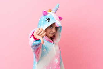 Little caucasian woman wearing a unicorn pajama isolated on pink background showing thumb down with...