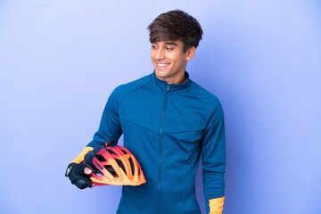 Young cyclist caucasian man isolated on purple background looking to the side and smiling