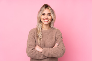 Teenager blonde girl wearing a sweater over isolated pink background keeping the arms crossed in...