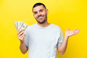 Young caucasian man taking a lot of money isolated on yellow background with shocked facial...