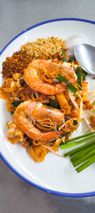 Pad Thai with fresh shrimp in a white plate with blue edges on a stainless steel table.