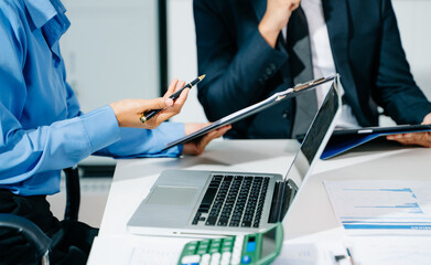 Business documents on office table with smart phone and laptop and two colleagues discussing data...