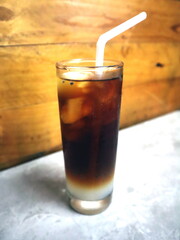 A tall glass of iced coffee with milk, featuring a clear layer separation and a white bendy straw, set against a wooden background.