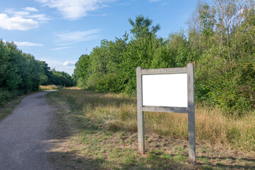 A blank interpretation sign in a country park with a track, trees and grass, with a blue sky.