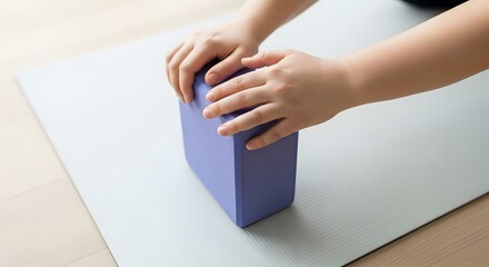 Obraz premium Hands positioning a purple yoga block on a gray exercise mat.