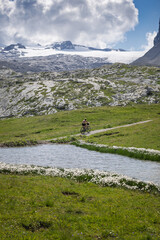 Cycliste en montagne, avec un étang, un chemin, des rochers et un glacier
