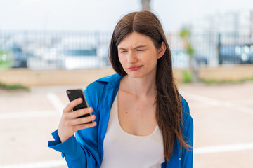Young pretty Ukrainian woman using mobile phone at outdoors with sad expression