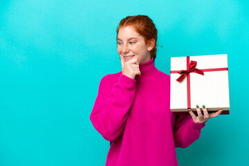 Young caucasian reddish woman holding a gift isolated on blue background thinking an idea and...
