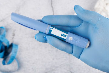 Blue gloved hand holding semaglutide injection pen on concrete surface, top view representing diabetes care and hormone treatment