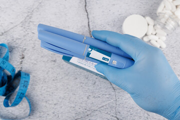 Top view of blue gloved hand with semaglutide injector on concrete, medical flatlay for diabetes, hormone care and obesity control