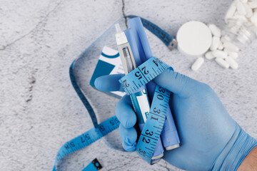 Top view of semaglutide injector with measuring tape and gloved hand on concrete, medical flat lay for health and hormone therapy