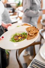 Close-up of gourmet beef tartare with raw egg yolk, mustard seeds, microgreens, and toasted bread on a white plate in a restaurant setting.