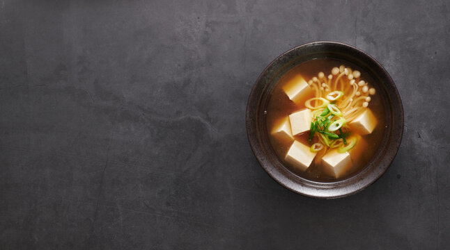 Japanese Miso Soup with Tofu and Enoki Mushrooms, on black background, top view, copy space