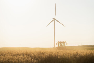 Agricultural tractor is working on the field with wind turbines