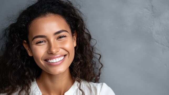 Close up face of young woman with beautiful smile isolated on grey wall with copy space. Successful multiethnic girl. Latin woman looking at camera against gray wall with a big whitening teeth smile.