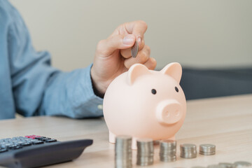 Young woman saving money monthly expenses putting coin in to piggy bank on the table.