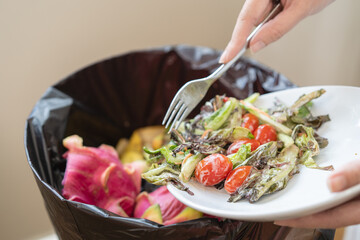 The housewife is throwing the leftover food from the meal into the bin