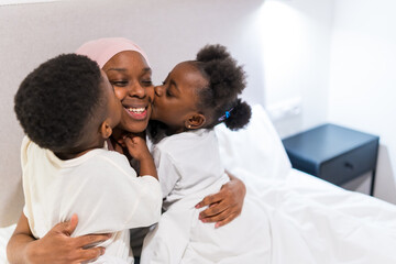 Children kissing smiling mother with cancer in bed