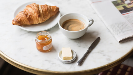 Parisian breakfast flat lay with a fresh croissant, café au lait, and jam on a classic white marble bistro table.