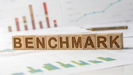 Wooden letters forming "BENCHMARK" with defocused performance comparison charts
