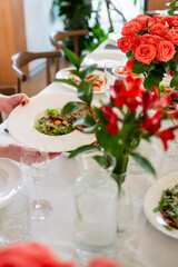 Elegant restaurant table setting with gourmet food, red flowers, and stylish glassware, creating a luxurious and inviting fine dining atmosphere.