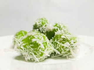 Traditional Indonesian klepon, green glutinous rice balls coated with grated coconut. A sweet snack filled with palm sugar, served on a white plate.