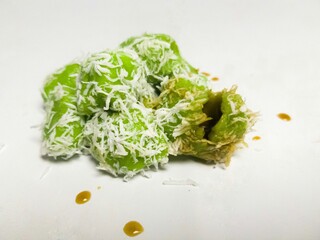 Close-up of traditional Indonesian klepon, glutinous rice balls coated with grated coconut and filled with melting palm sugar, served on a white surface.