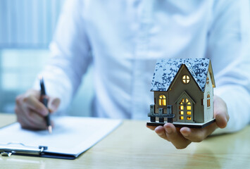 Real estate agent and customer discussing a contract with house model on table. Concept of home...