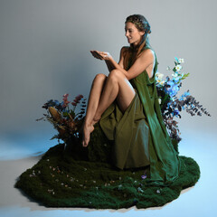 fantasy portrait beautiful female model wearing green fairy gown costume. sitting pose on moss...