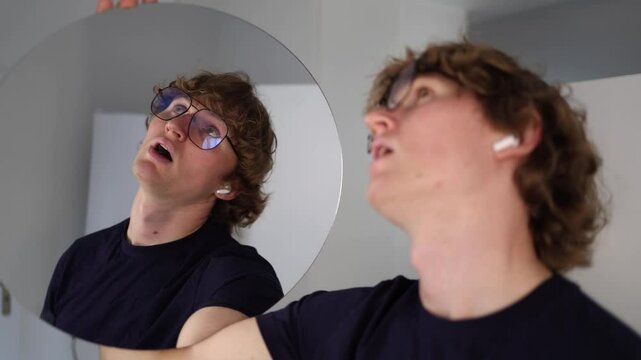 Young man makes a pouty face at his reflection acting overly dramatic or playfully disappointed in what he sees in the mirror