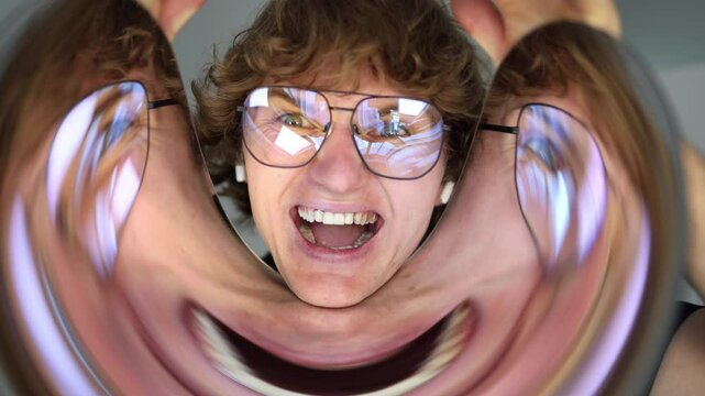 Young man with curly hair laughs wildly while looking at his surreal reflection in a distorted mirror creating a bizarre moment of pure amusement and unfiltered expression