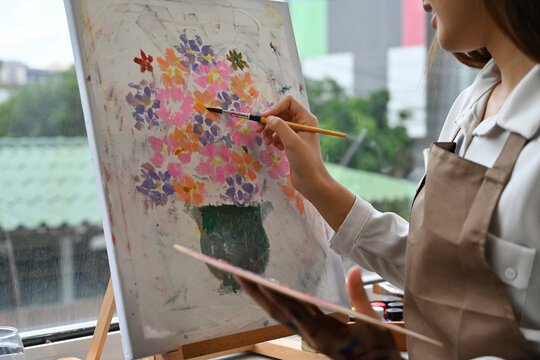 Close-up of a woman's hands painting flowers with acrylics, focusing on artistic technique and brush control in a bright studio