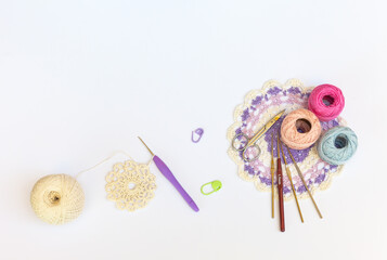 Process of knitting openwork round napkin with crochet hook. Set of hooks, skeins of cotton colored yarn, scissors and lace three-color doily on white background. Copy space, flat lay, close-up