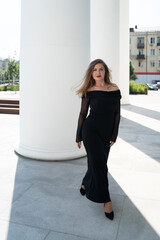 Obraz premium Beautiful girl in a black dress against the background of white columns