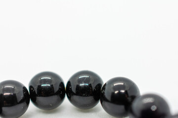 Black bracelet with a shiny surface. The bracelet is made of black beads and is placed on a white...