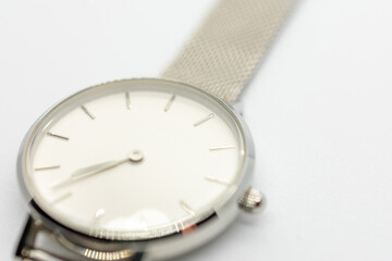 Silver watch with a white face sits on a white background. The watch is simple and elegant, with a...