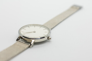 Silver watch with a white face sits on a white background. The watch is simple and elegant, with a...