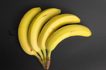 Four ripe bananas arranged artistically on a dark surface, showcasing their vibrant yellow color...