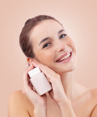 Smiling young woman with makeup holding a plastic cosmetic jar of face cream near her face....